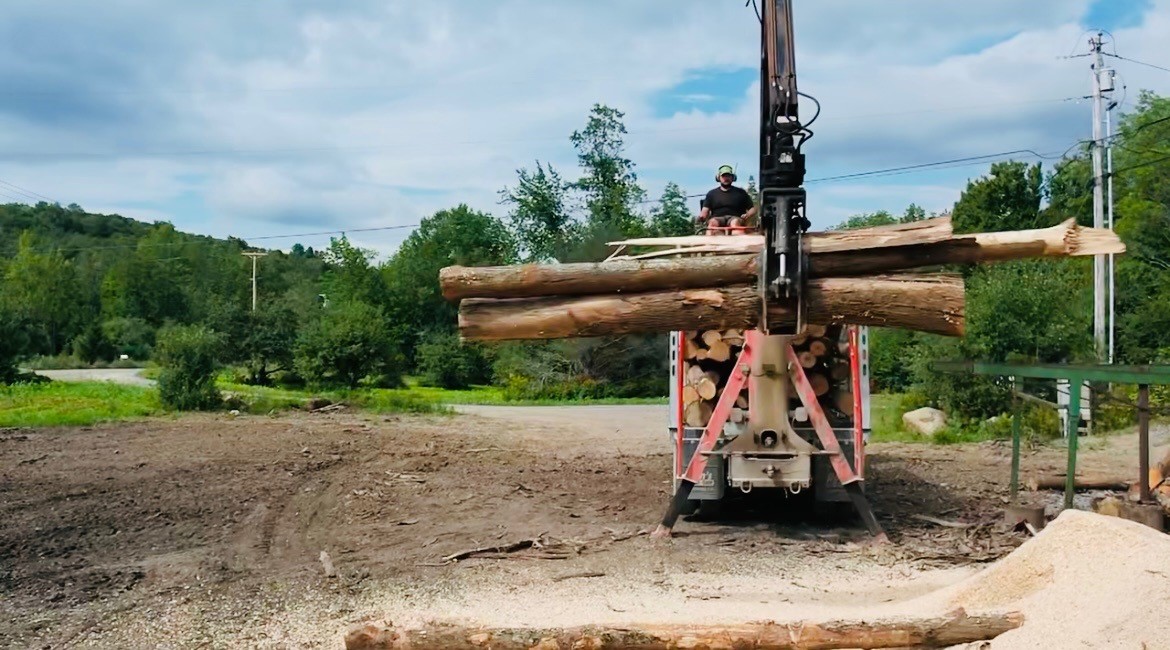 Logs are on a loader and there is a blue sky and green mountains in the background