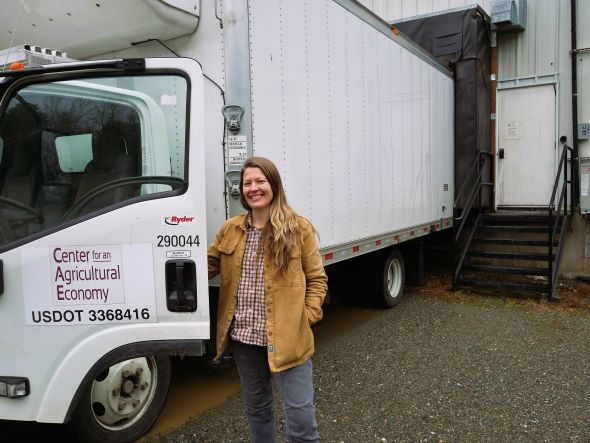 Corey Hennessey stands next to an open door of a white truck that says Center for an Agricultural Economy on the door. Truck is backed into loading dock