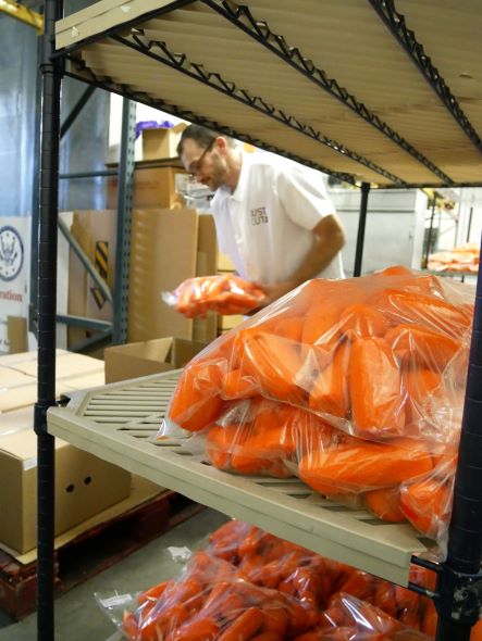 Shelf with bags of clean and cut carrots in foreground. In background, a person puts bags of carrots into boxes.