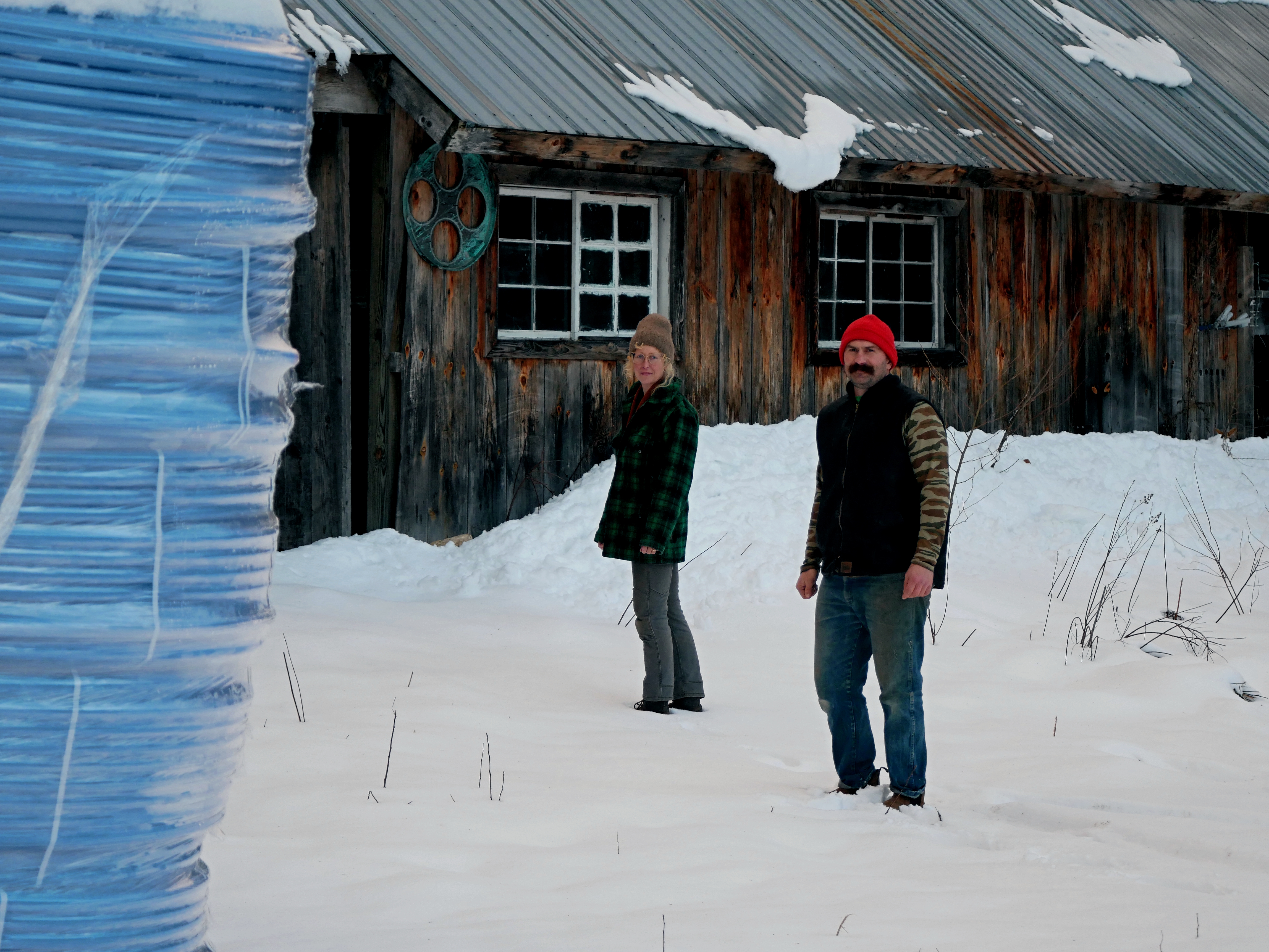 A coil roll of sap lines in the foreground. Chris and Kari walk into a building in the snow in the background.