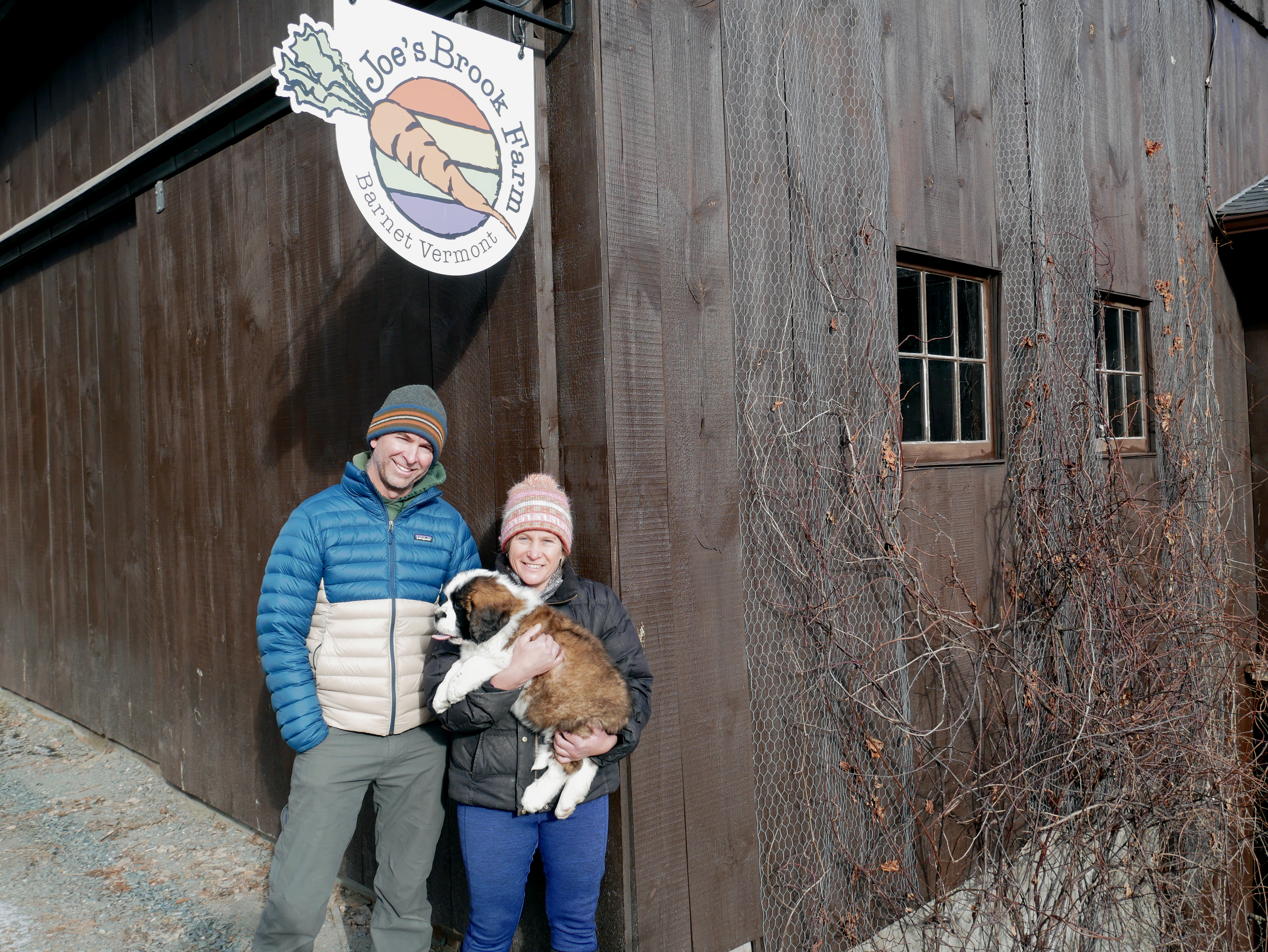 Eric and Mary Skovsted stand with their dog in front of their farm sign