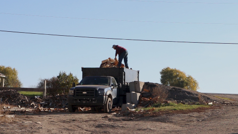 A person stands on top of a dump truck full of firewood