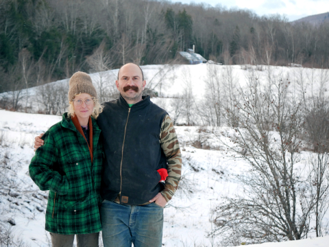 Kari Anderson and Chris Redder stand outside in the snow in front of a field