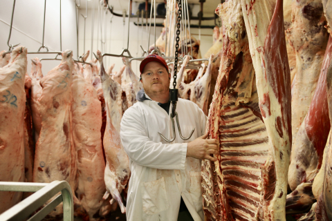 Ryan Cushing stands among hanging skinned carcasses for meat cutting. Photo credit Steve James, Addison Indpendent.