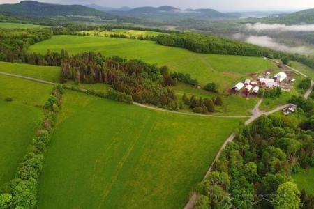 Aerial view of Molly Brook Farm with lush fields, farm buildings, and clouds hanging low over distant hills.