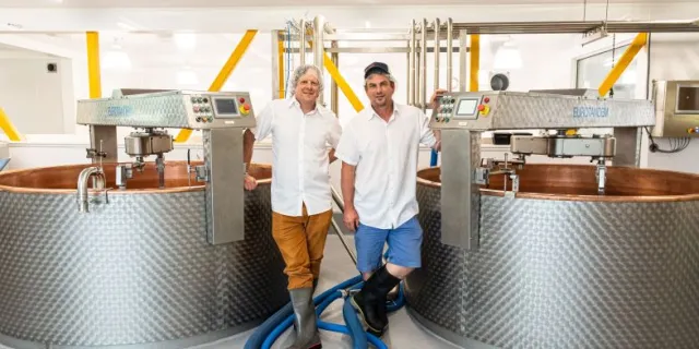 Kehler brothers standing next to cheesemaking equipment.