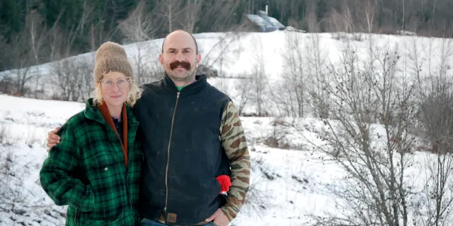 Kari Anderson and Chris Redder stand outside in the snow in front of a field