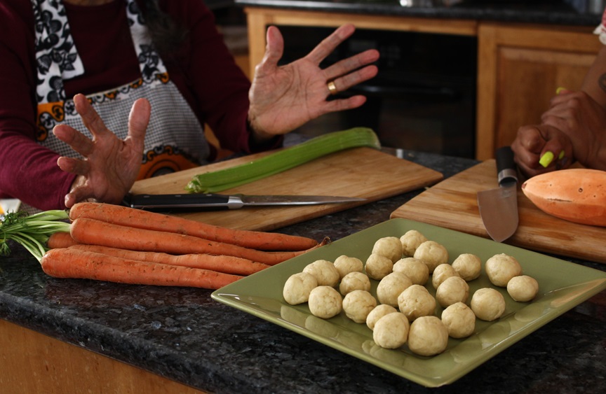 Table with whole carrots and a tray of dumplings. A person's hands are visible on the left side of the frame.