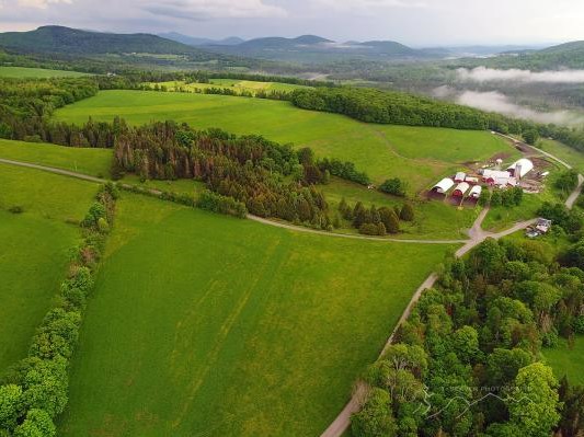 Aerial view of Molly Brook Farm with lush fields, farm buildings, and clouds hanging low over distant hills.
