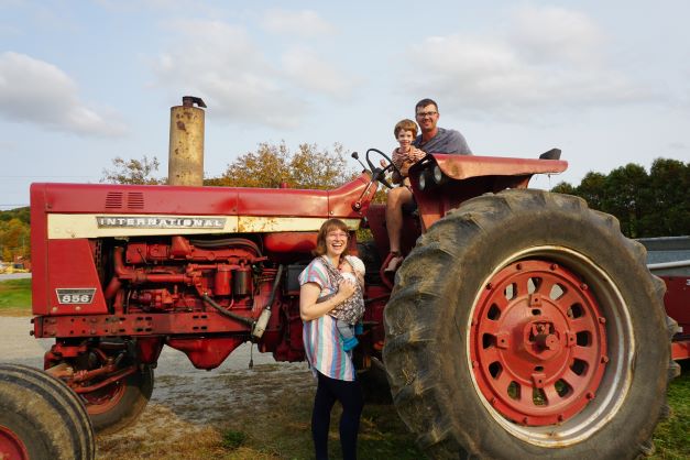 A family of a mother, father, and 2 children sit on a large red tractor
