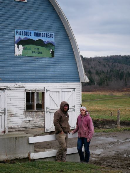 Chet and Renee Baker in front of a blue and white barn with a sign that says Hillside Homestead
