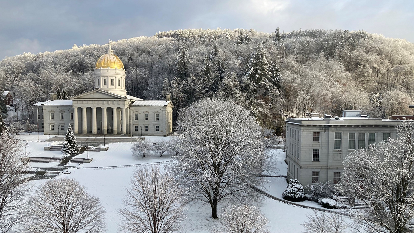 Vermont Statehouse in winter snow with trees in foreground