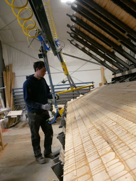 A person stands next to a machine clamping glued wood