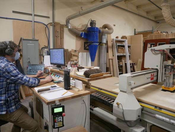 A person runs a computer next to a large table wood machine with a butcher block