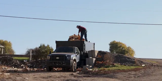A person stands on top of a dump truck full of firewood