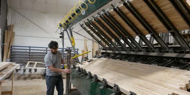 A person stands next to a large piece of equipment that is clamping glued planks of wood together