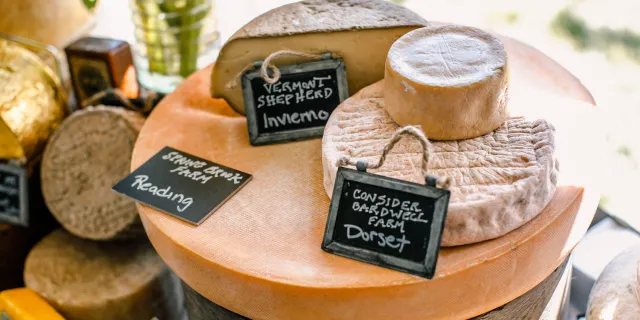 Table with VT cheese wheels and wax wrapped cheese. Label says "Spring Brook Farm, Reading" "Vermont Shepherd Invierno" "Consider Bardwell Farm, Dorset"