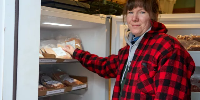 A young woman in a red plaid jacket opens a freezer full of chicken